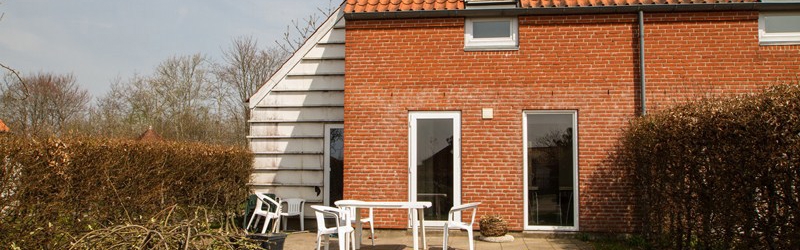 Søvænget huset fra haven af hvor en terrasse er med et bord og stole og en lille græsplæne
